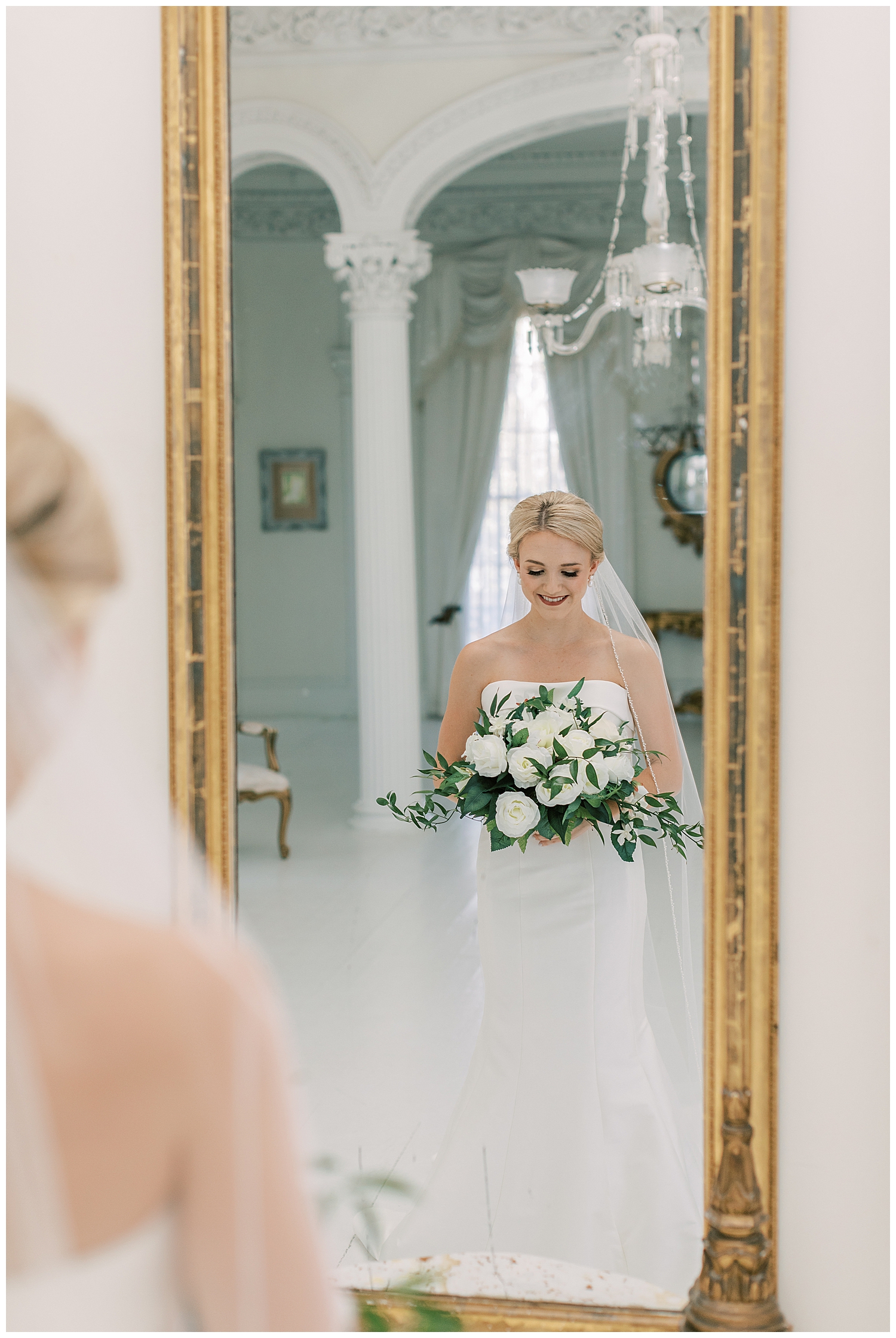 A bride looks in a mirror in a white room.