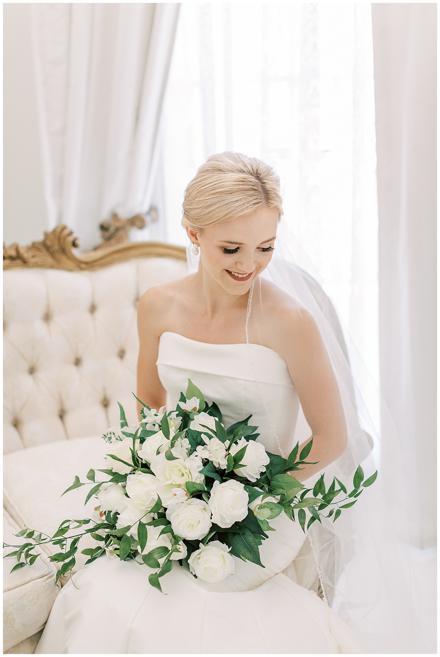 A bride sits on a vintage sofa in a white room.