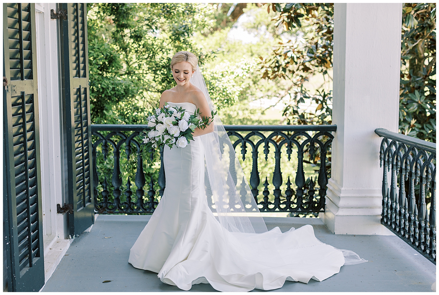 A bride looks down at her bouquet on the porch of Nottoway Plantation in Louisiana.