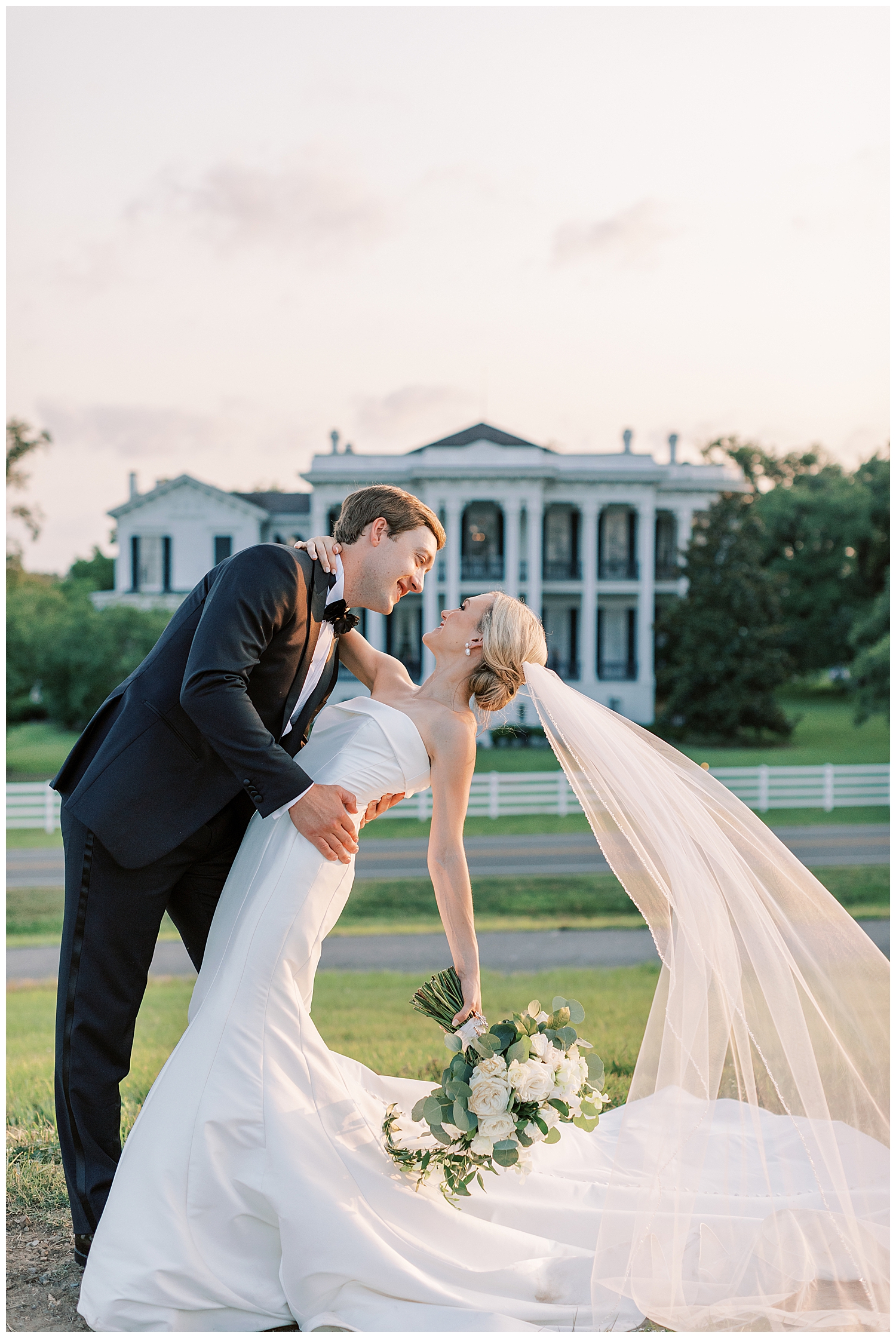 A husband and wife embrace each other while standing before Nottoway Plantation at sunset.