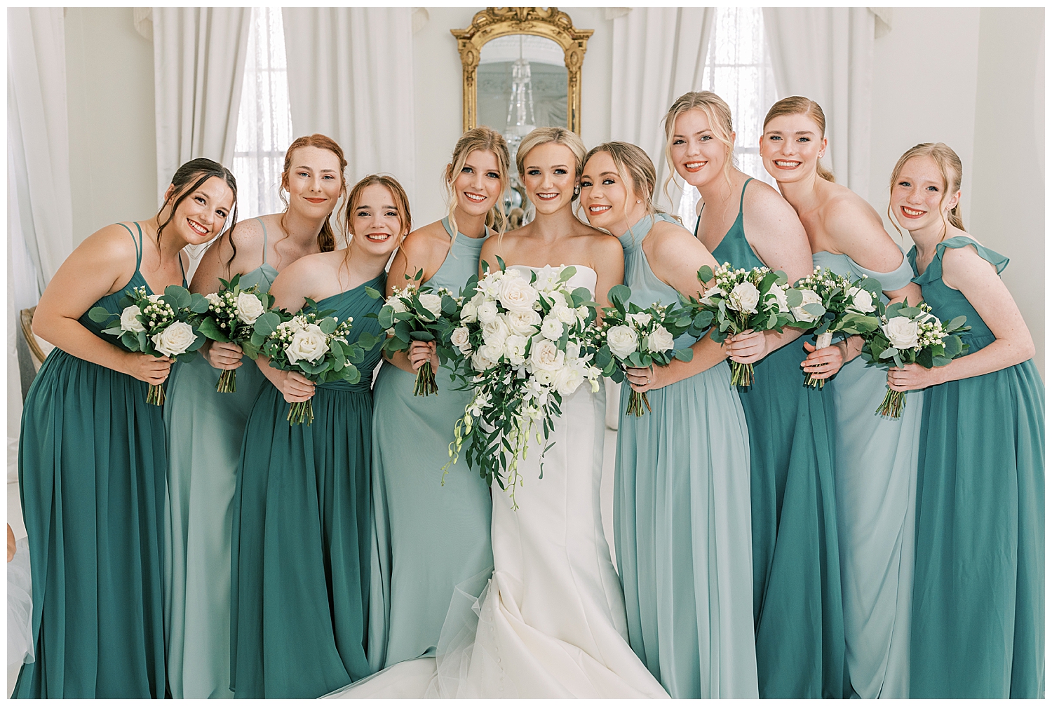 A bride stands with the bridesmaids in a white room.