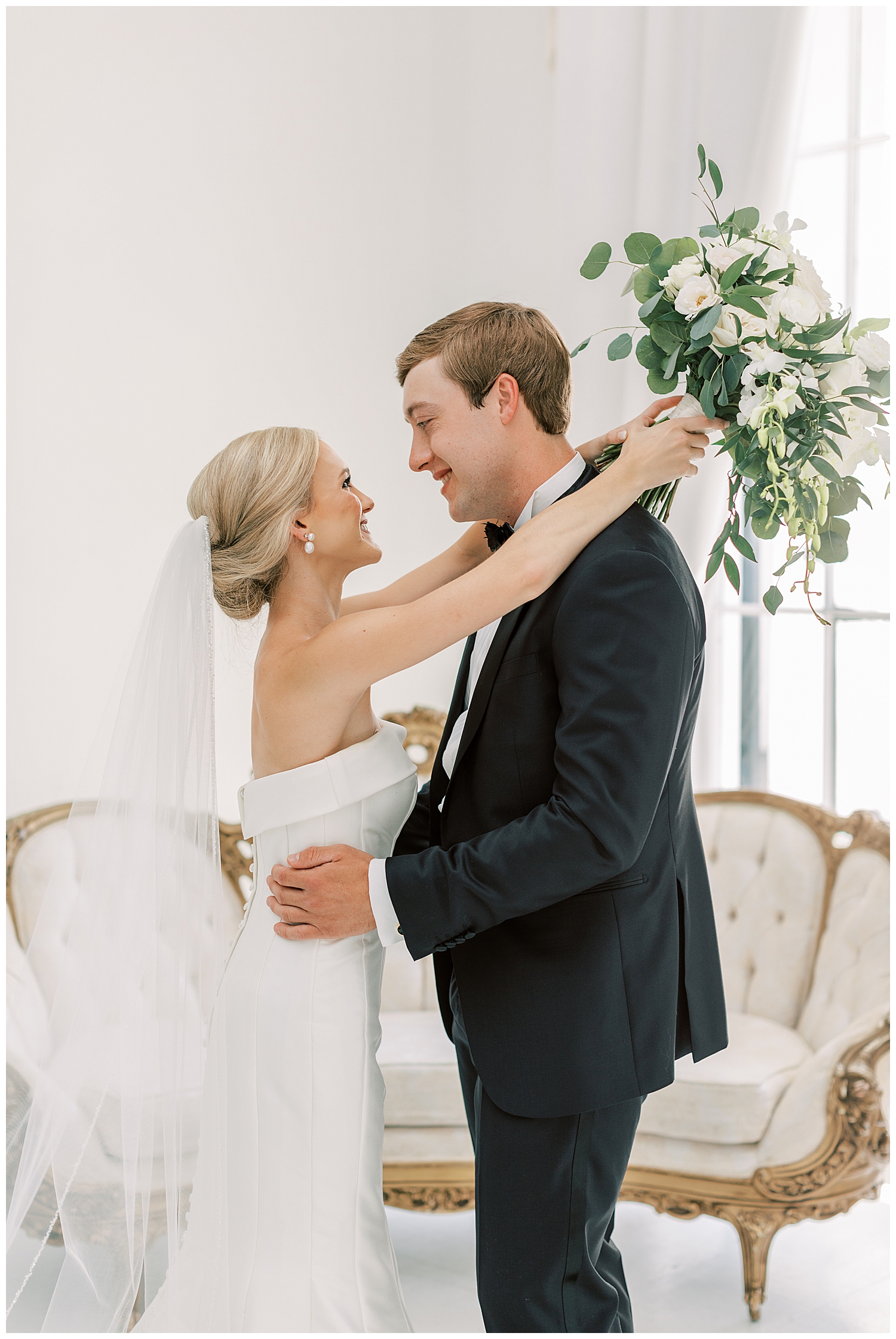 A bride and groom embrace each other in a white room.