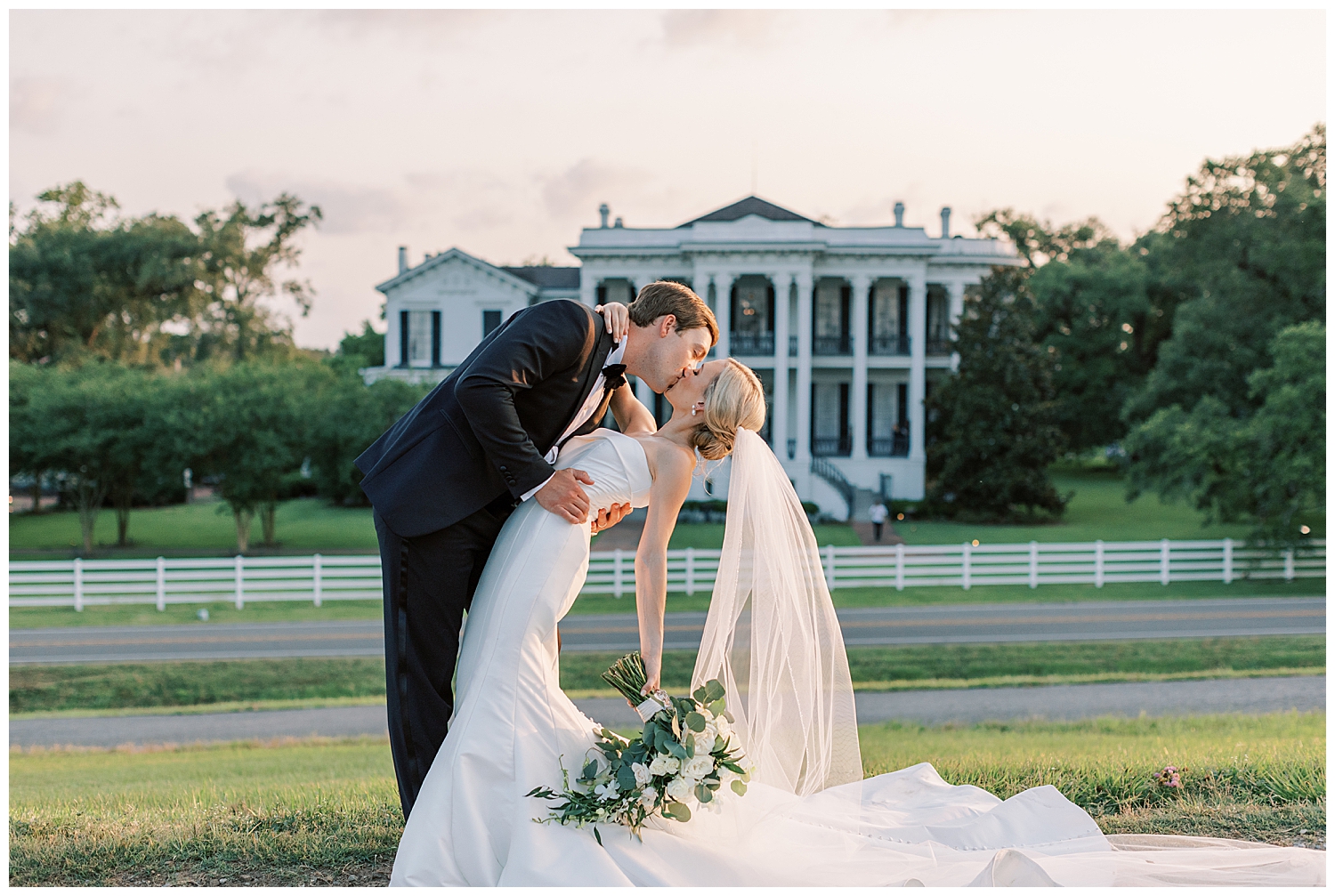 A husband and wife kiss while standing before Nottoway Plantation at sunset.