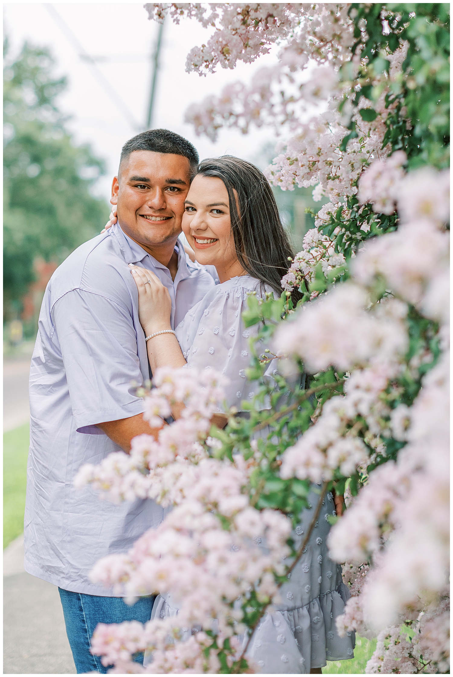 A joyful couple in Hattiesburg stand by a huge flowering bush.