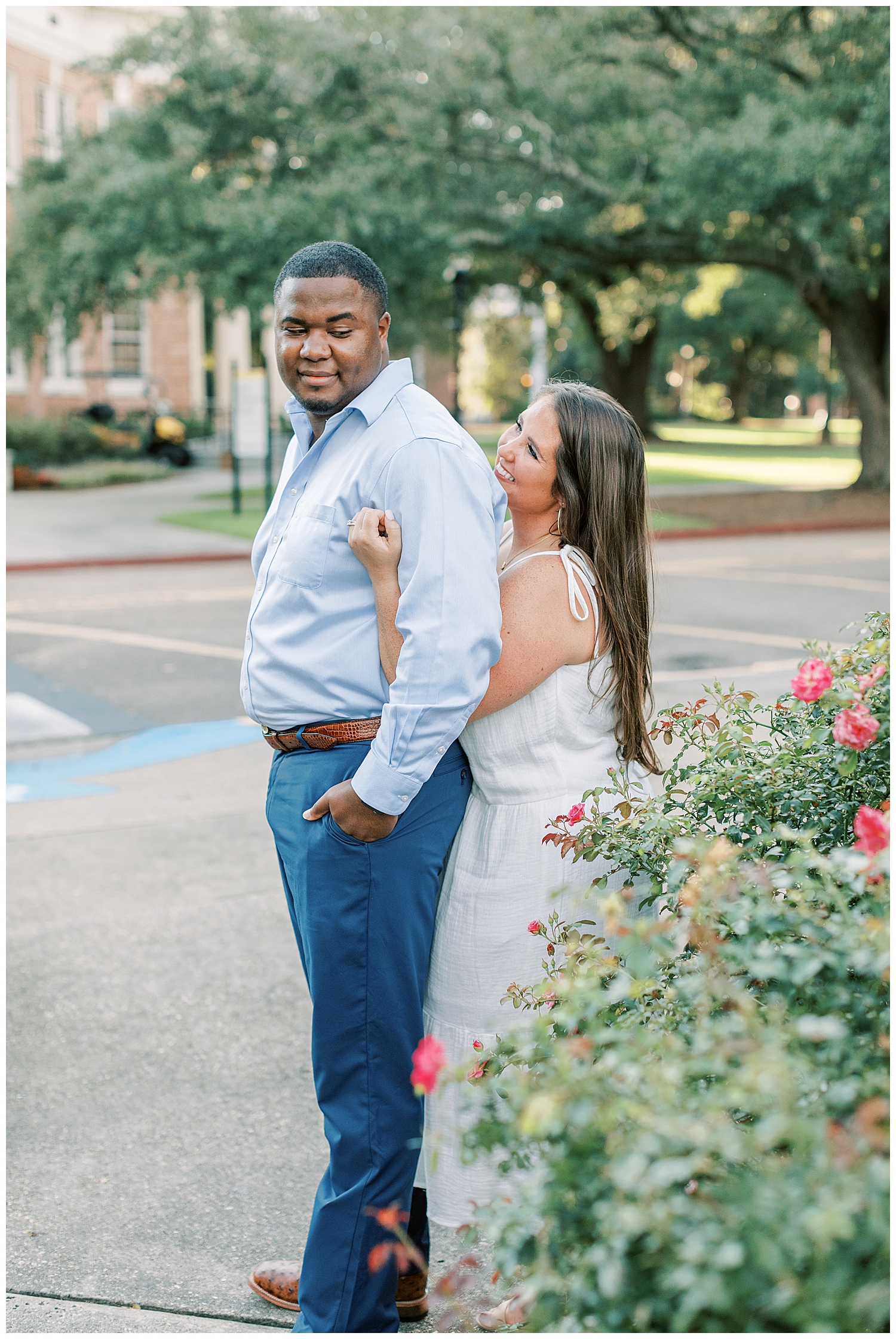 An engaged couple hugs in front of a rose bush.