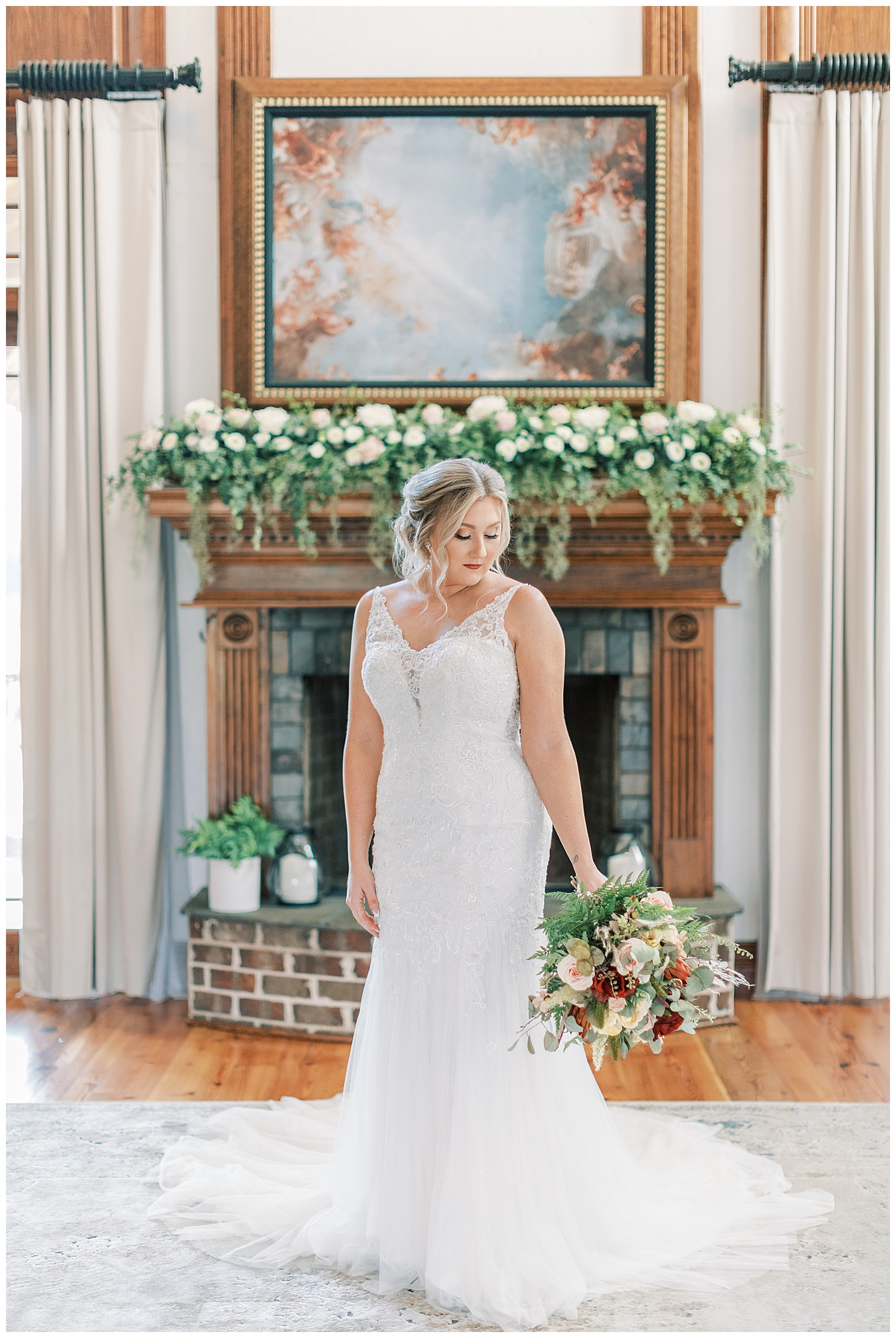 A bride stands in front of the fireplace.