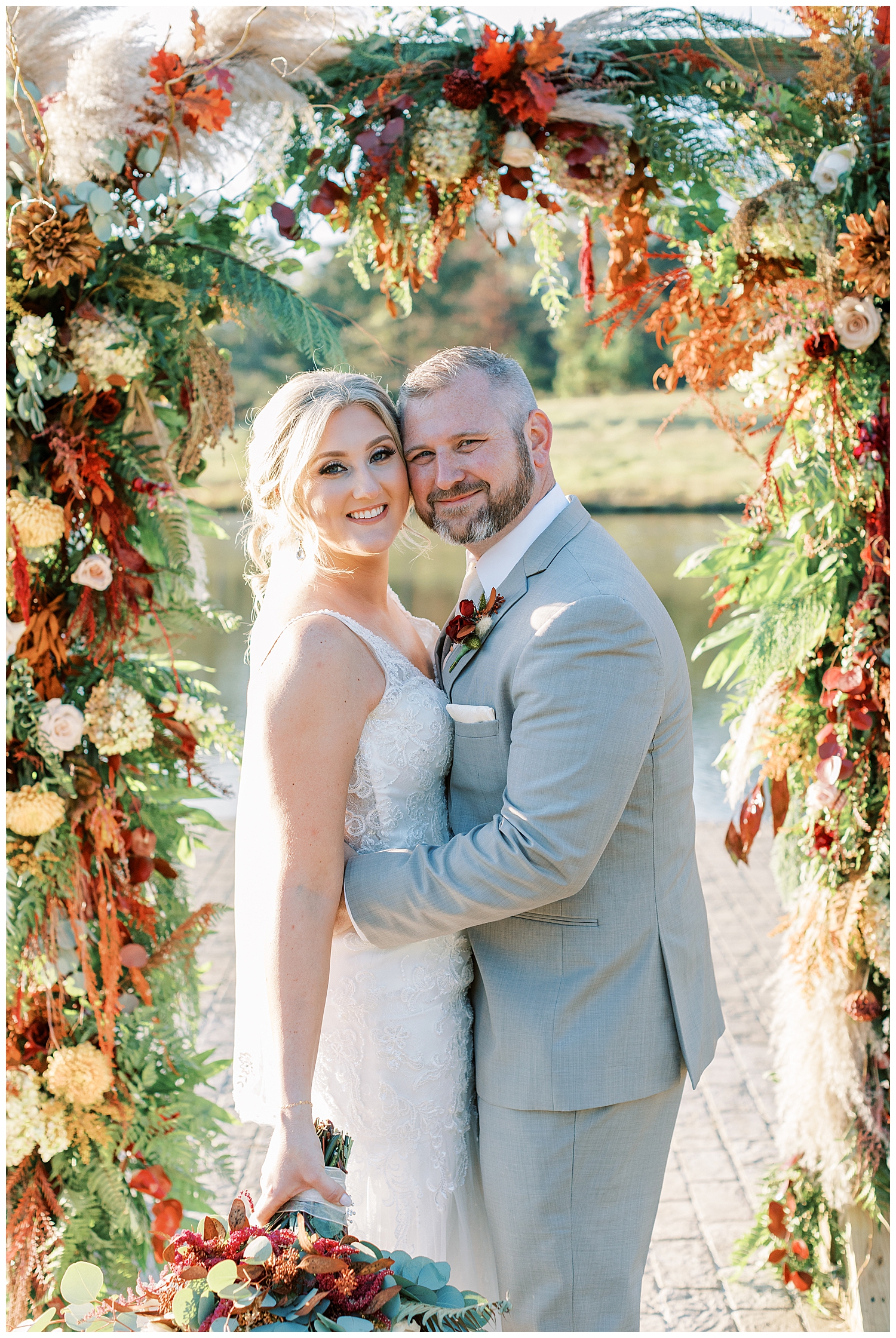 A husband and wife smile in front of a floral arch.