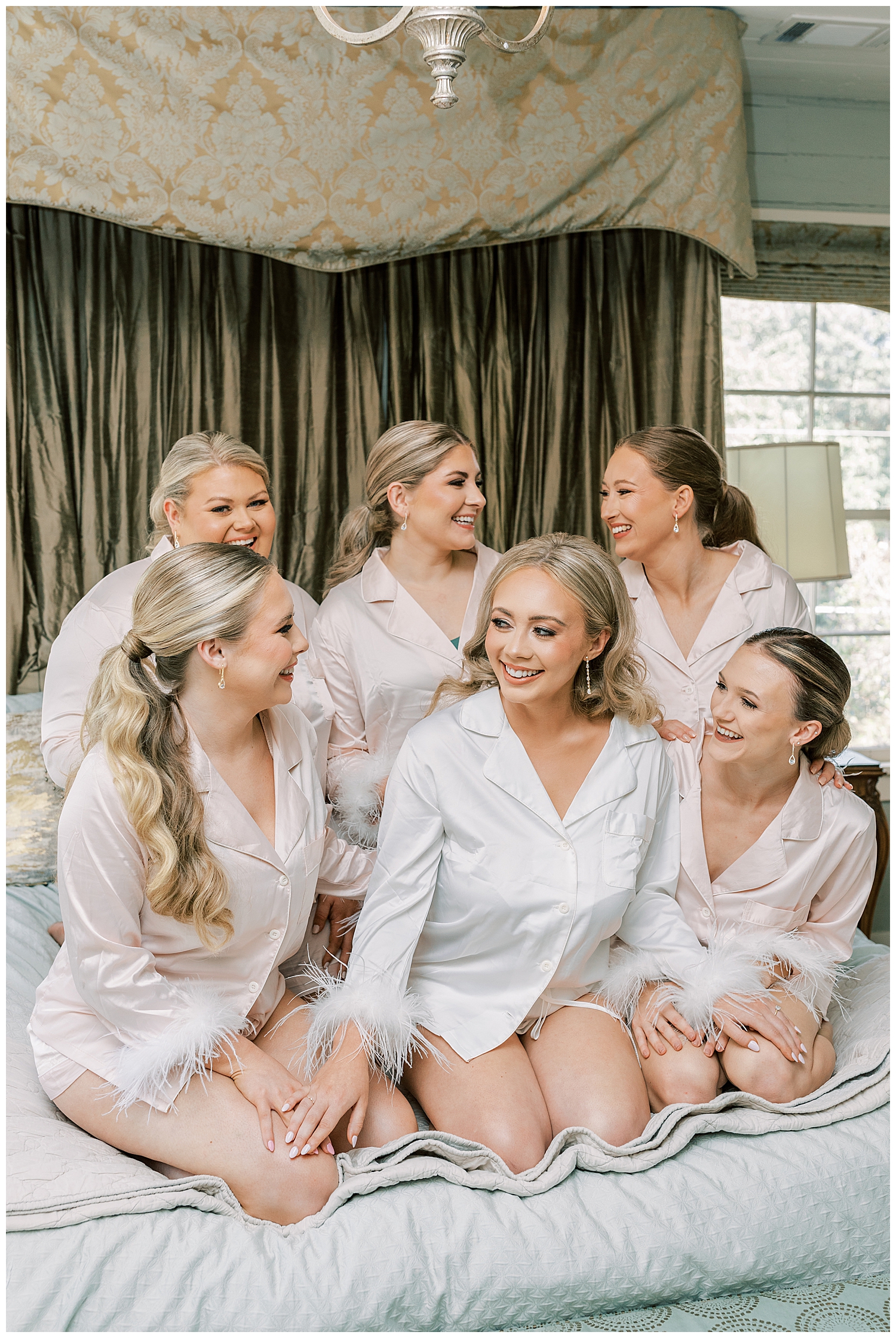 A bride sits on the bed with the bridesmaids featured in Signature Magazine.