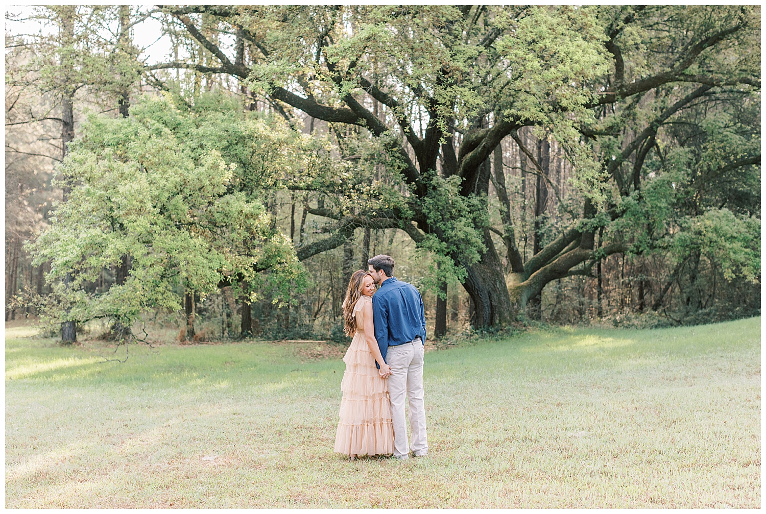 A couple kisses in front of an oak tree for their spring engagement photos.