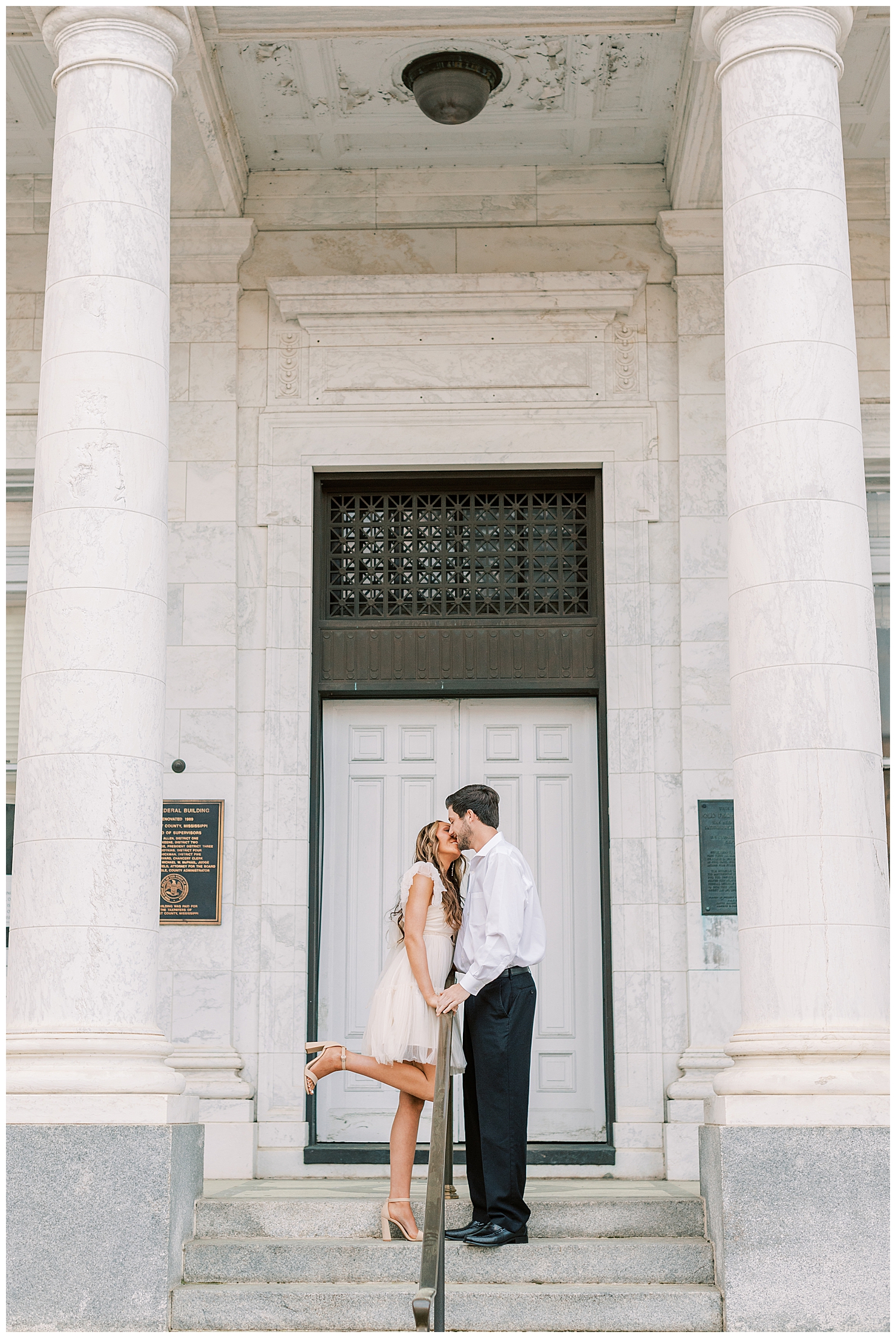 A couple kisses between columns for their spring engagement photos.