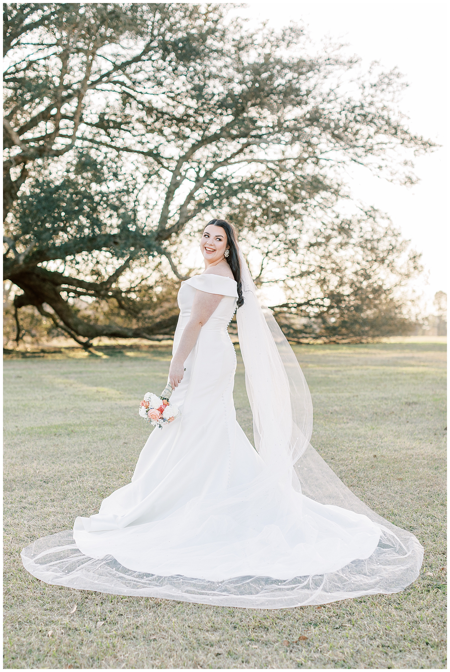 A bride looks over her shoulder while standing in front of an oak tree.