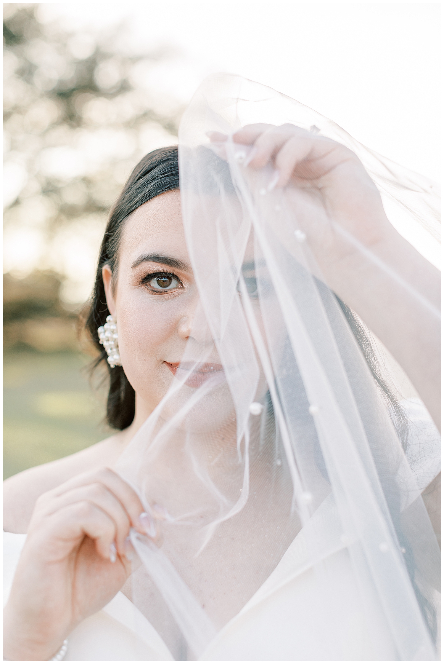 A bride holds the pearl veil over her face.