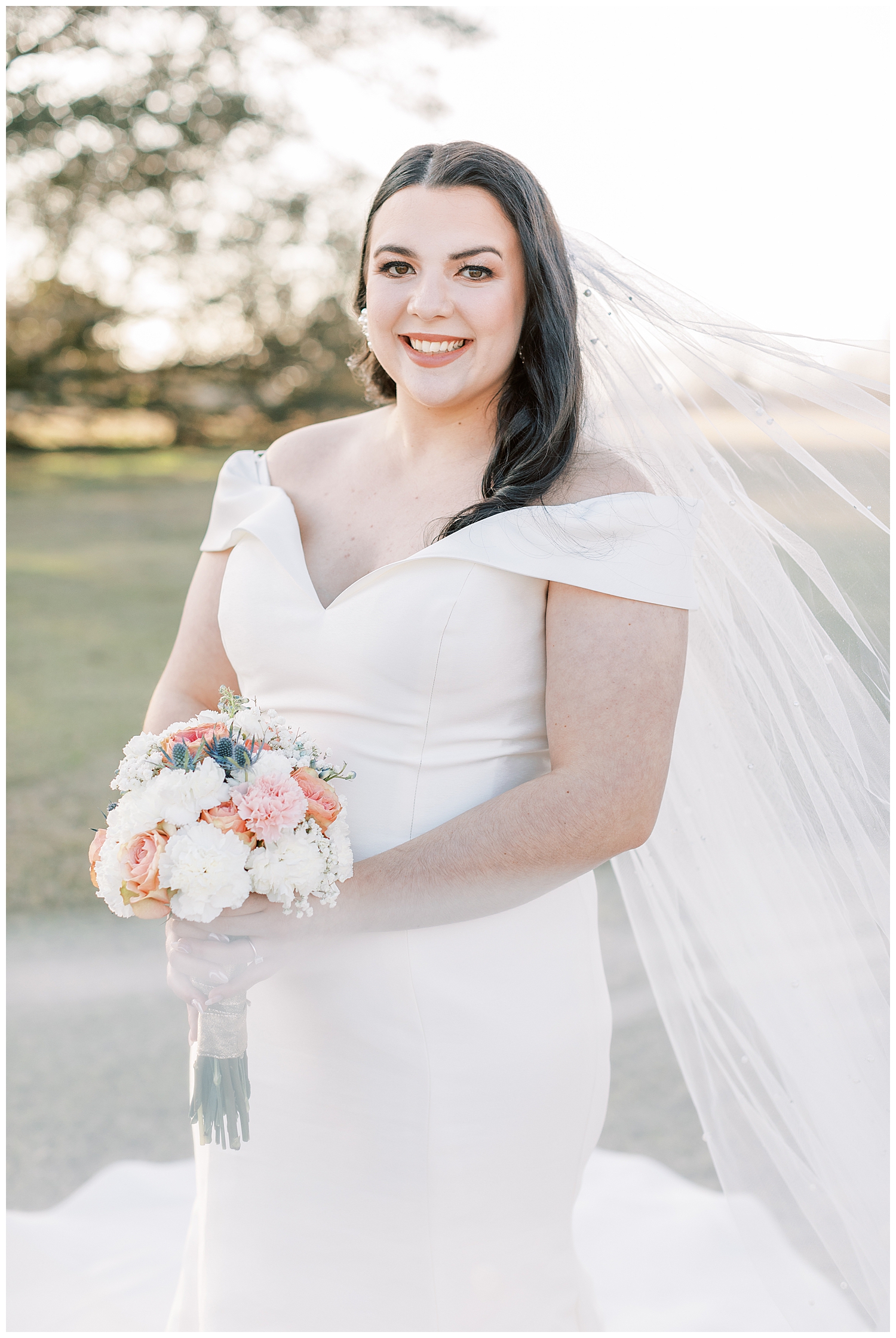 A bride holds her bouquet and smiles over her pearl veil.