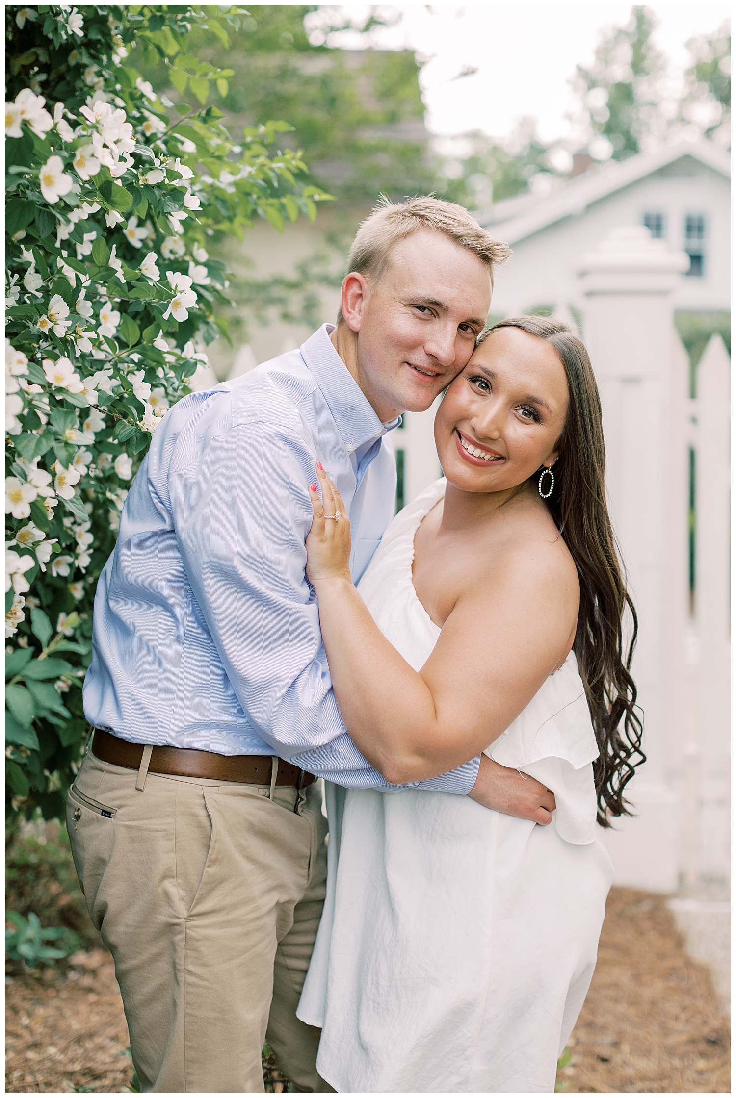 A couple smiles by a bush for their Hattiesburg engagement session.