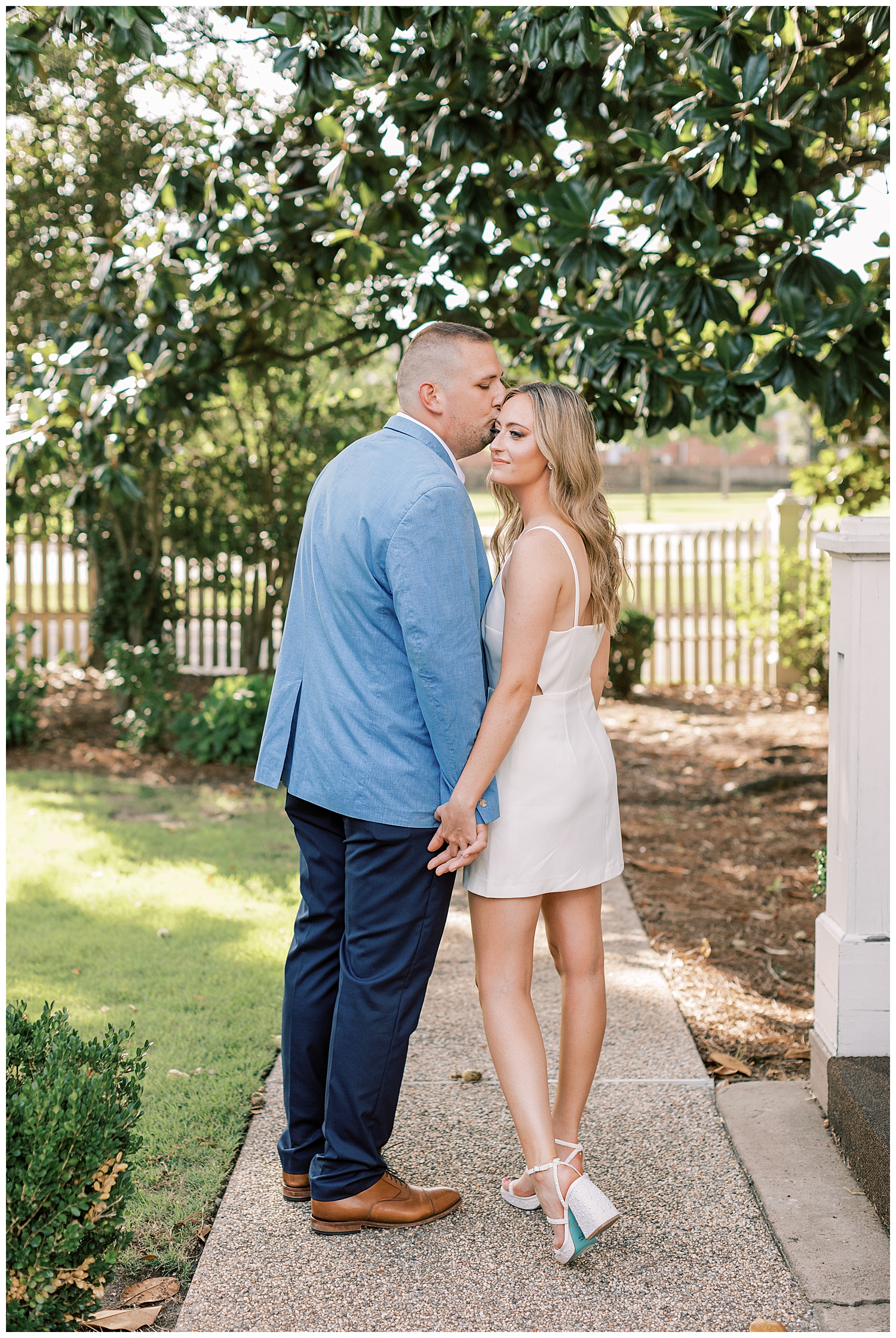 A couple kisses in front of a magnolia tree.