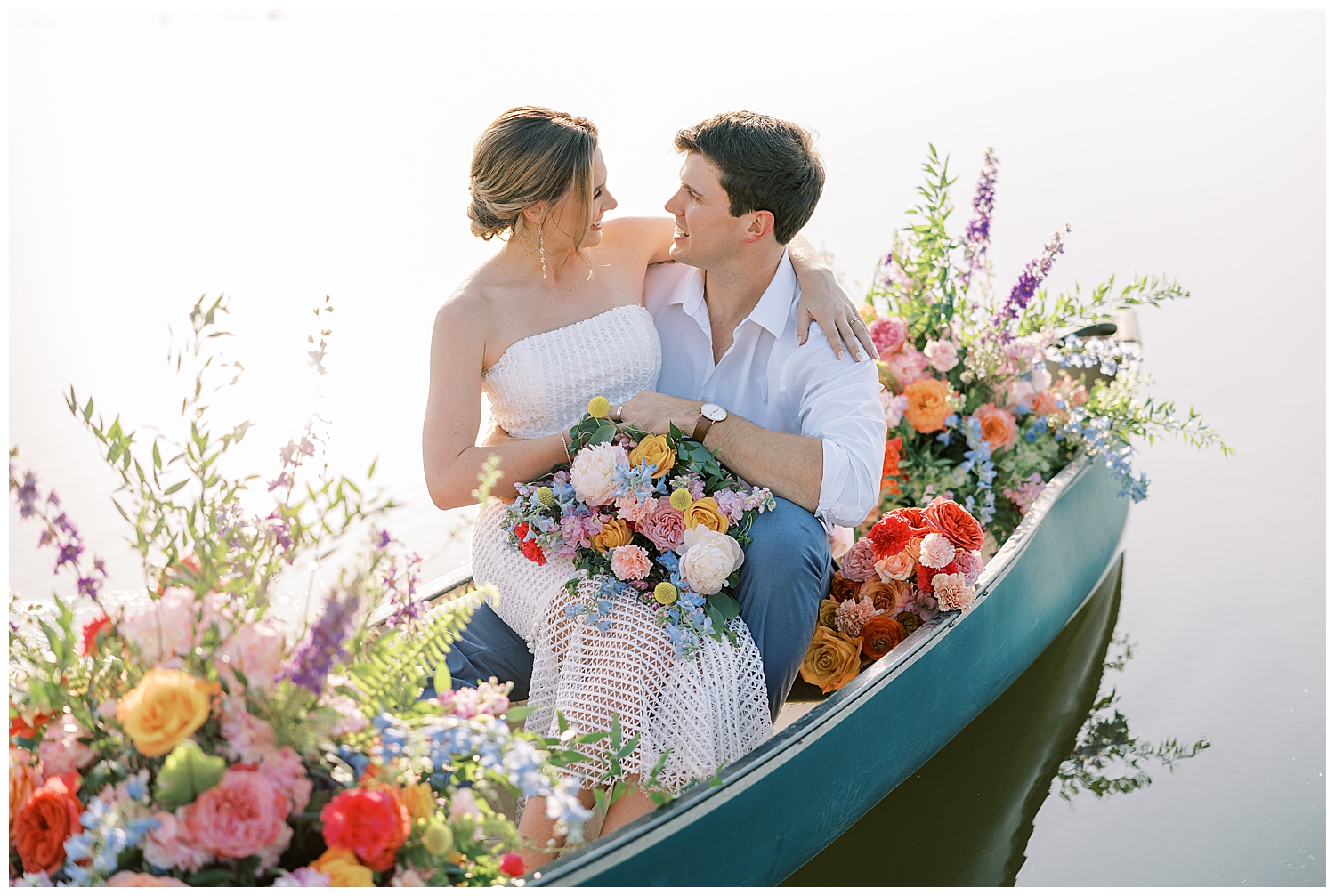 A couple rides in a canoe in the middle of a lake surrounded by flowers.